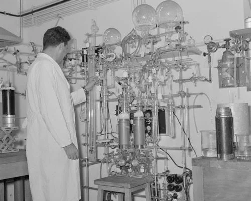 Archive photo of a chemist in a lab coat beside laboratory glassware